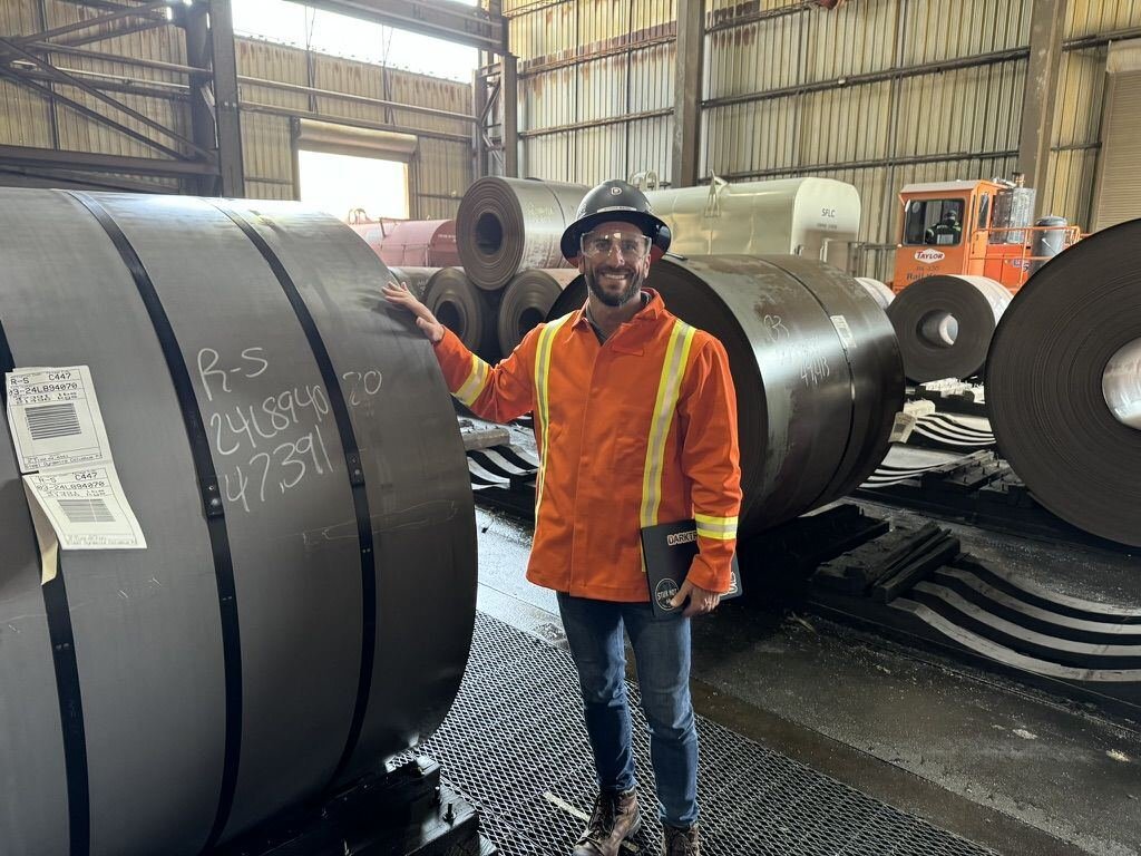 Jeffrey in PPE beside steel coils at a steel mill
