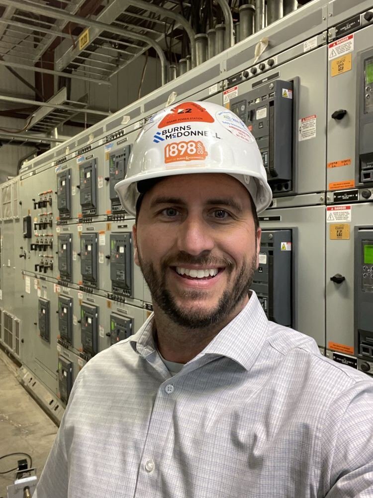 Jeffrey in a hard hat in front of power switchgear